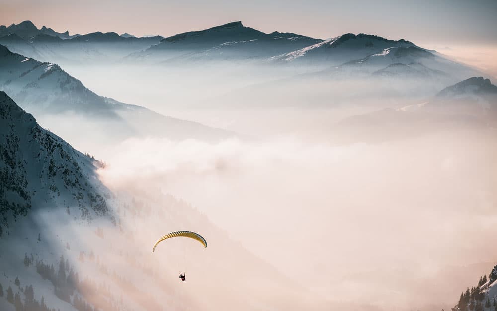 aerial-shot-person-parachuting-down-clouds-near-snowy-mountains