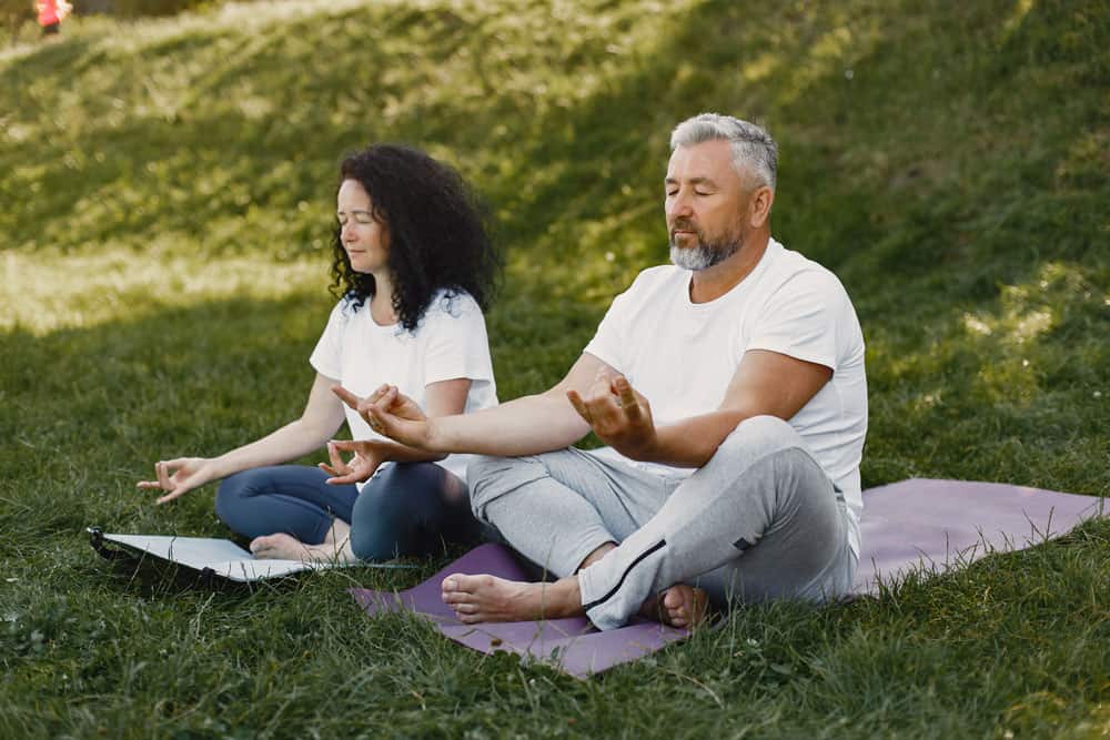 couple-is-doing-yoga-outdoors-stretching-park-during-sunrise-brunette-white-t-shirt-