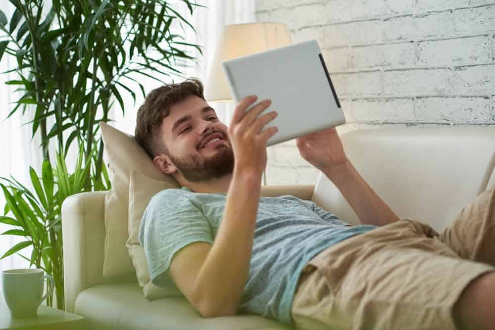 man lying on couch holding tablet