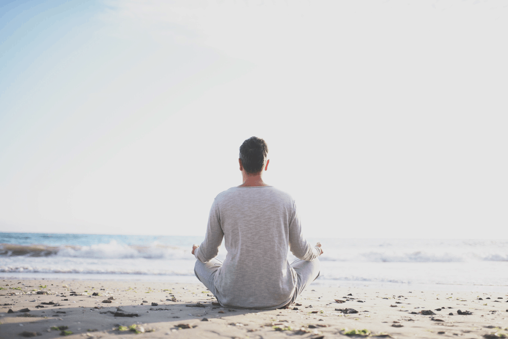 man meditating on beach