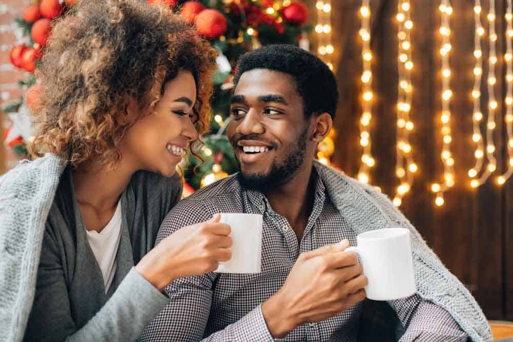 couple holding mugs near christmas tree