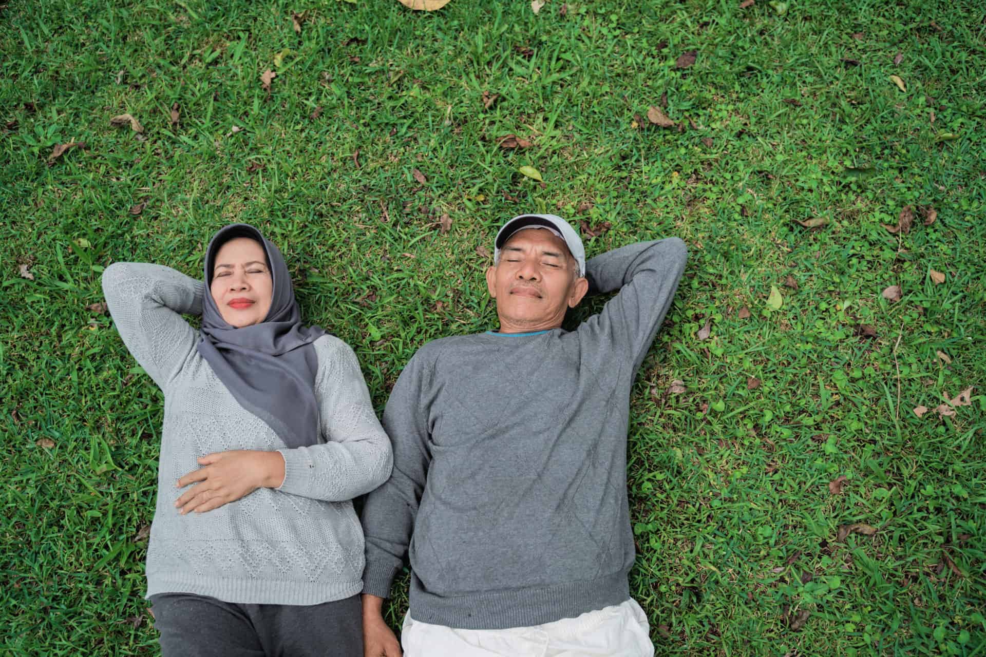 muslim senior man and woman relaxing and laying down on grass in the park
