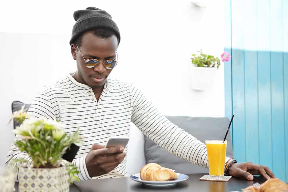 people-lifestyle-travel-vacations-modrn-technology-concept-handsome-dark-skinned-tourist-wearing-stylish-hat-sunglasses-texting-sms-mobile-phone-during-breakfast-sidewalk-cafe