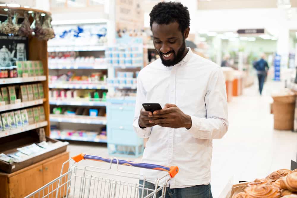 cheerful-black-man-typing-cellphone-grocery-store