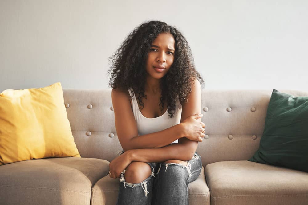 indoor-shot-beautiful-fashionable-young-mixed-race-woman-with-afro-hairstyle-sitting-couch-home-frowning-having-worried-sad