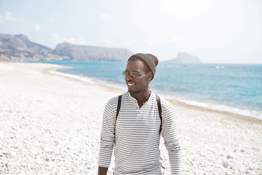 happy-young-afro-american-traveler-stylish-hat-sunglasses-having-nice-walk-along-seashore-enjoying-sunny-weather-beautiful-views-attractive-young-black-man-posing-sea-scenery